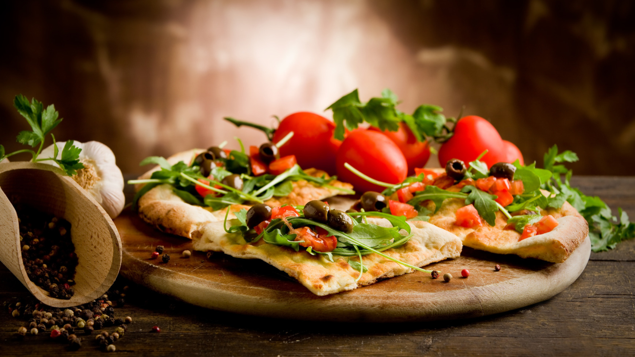 A pizza with tomatoes and greens on it.