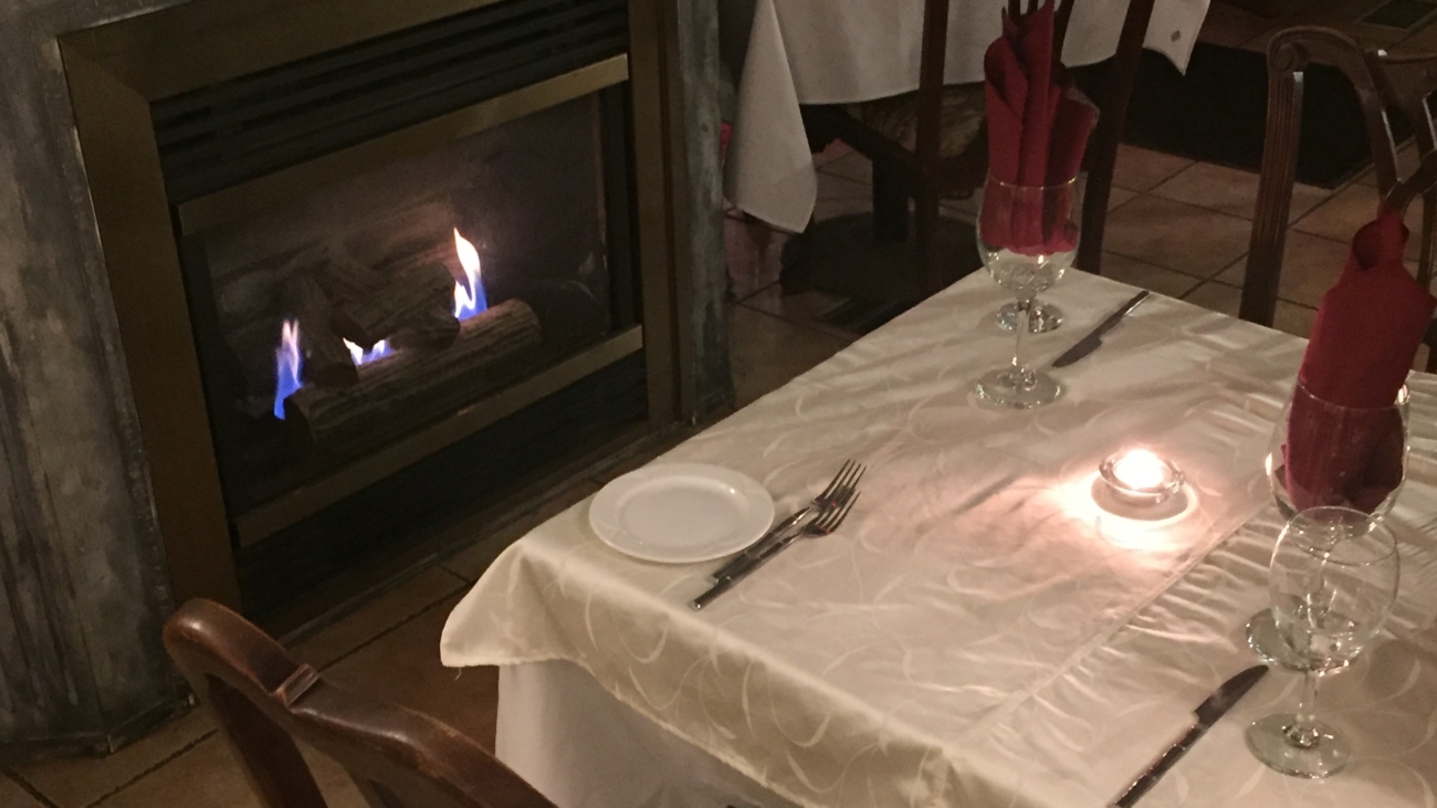 A table with candles and chairs in front of a fireplace.